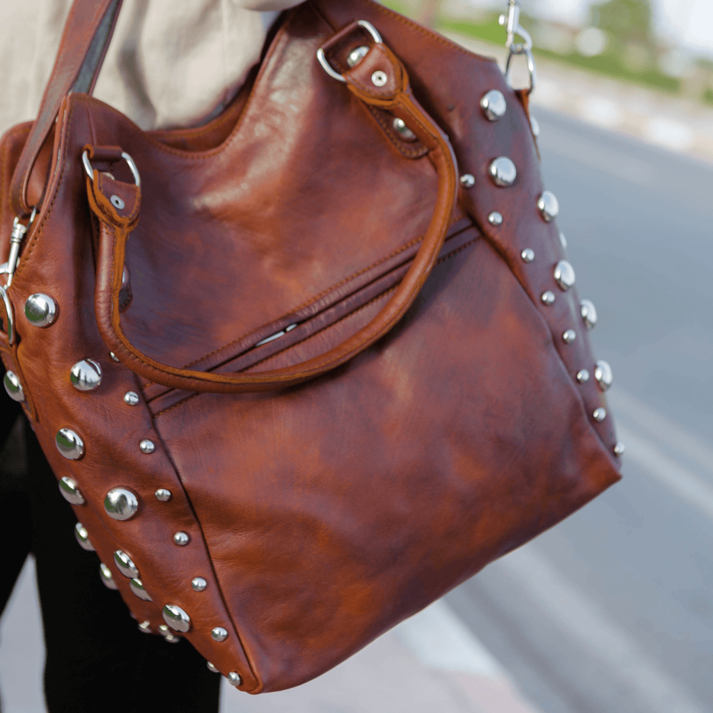 Brown leather handbag with studs held by a person on a blurred street background