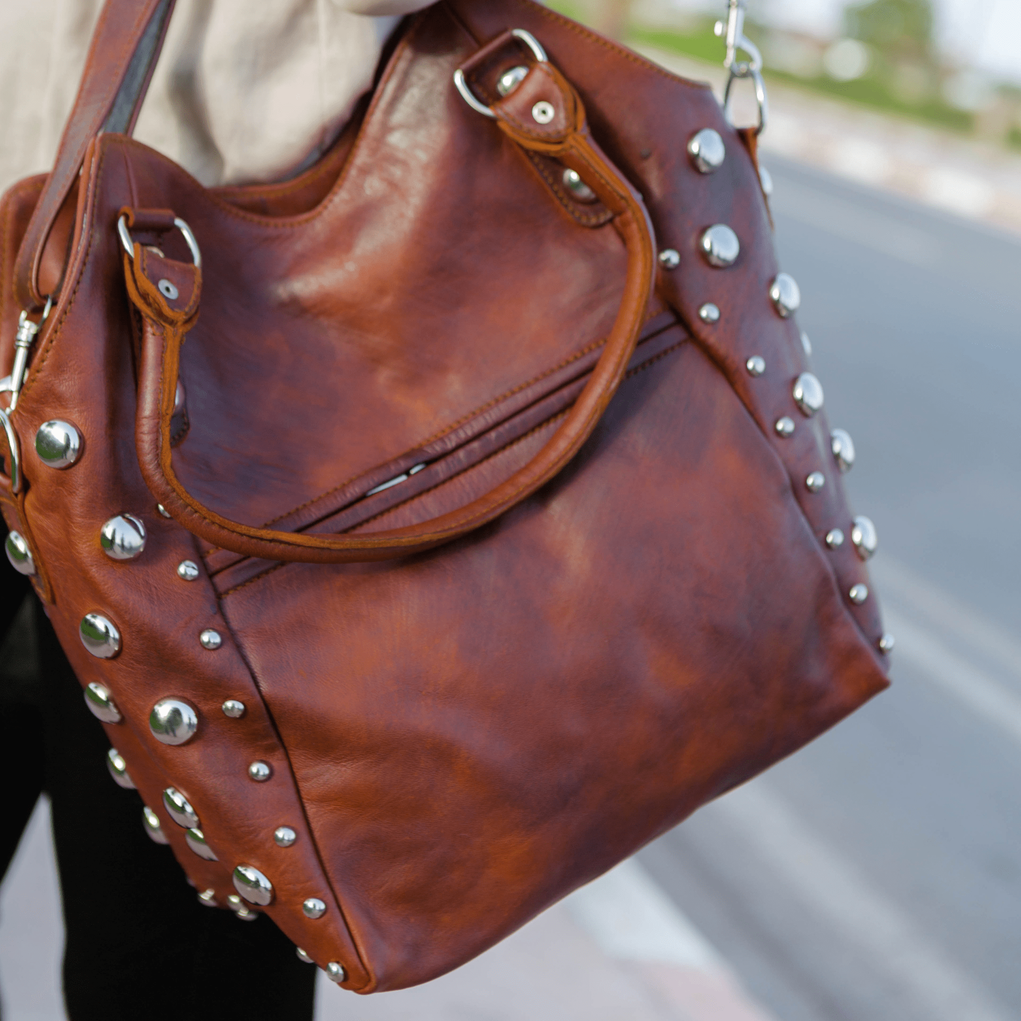 Brown leather handbag with studs held by a person on a blurred street background
