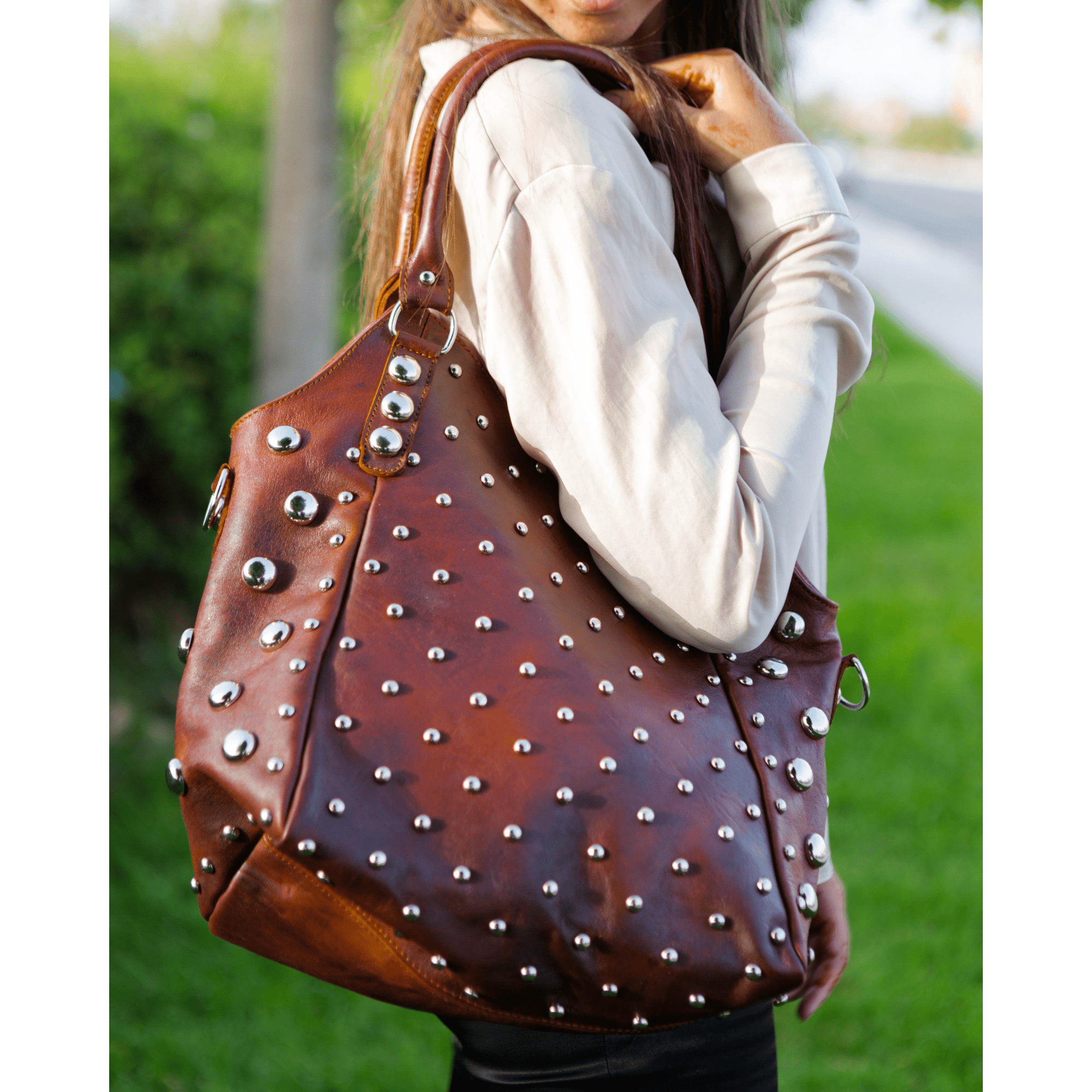 Brown studded handbag held by a person outdoors